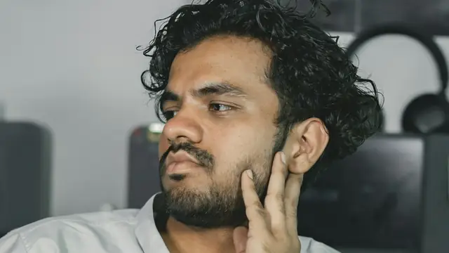 Homem com a mão perto do ouvido e da mandíbula